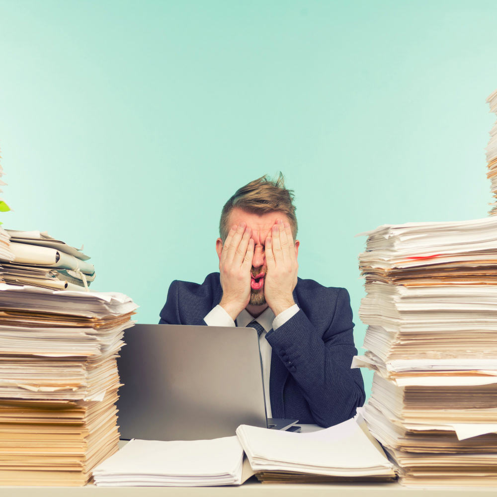 Contador agobiado entre pilas de papeles y documentos sin procesar