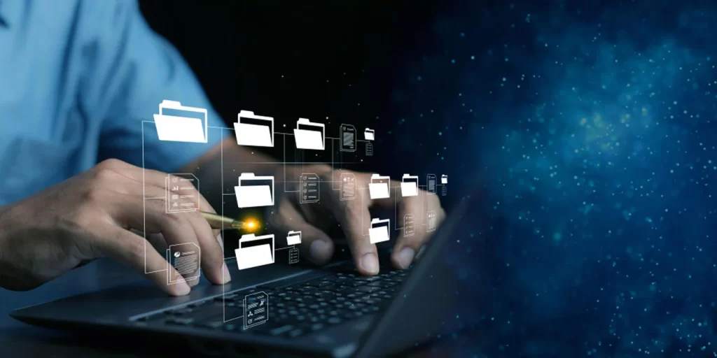 Manos escribiendo en un portátil mientras carpetas digitales flotan en la pantalla.