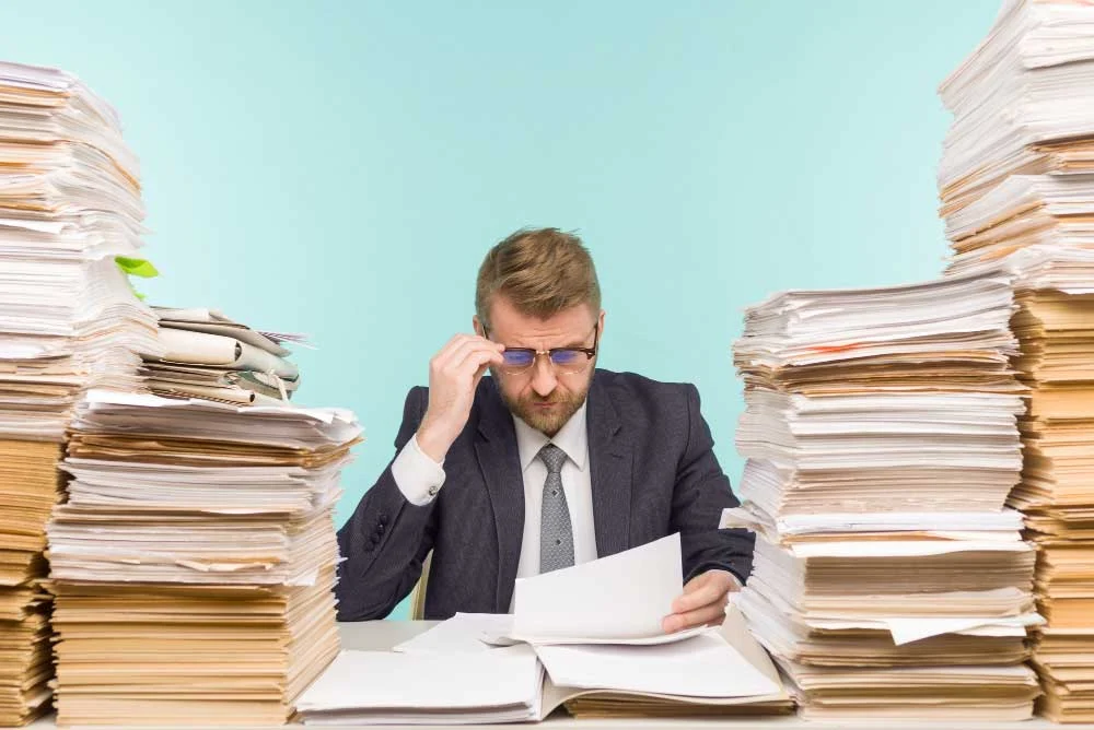 Empleado abrumado por montones de documentos, reflejando la necesidad de automatizar la recepción de documentos