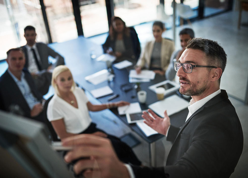 Líder señalando un panel mientras su equipo colabora en una mesa de trabajo