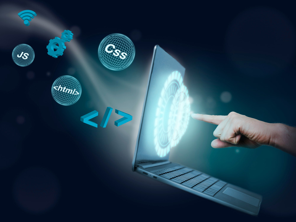 Mano interactuando con laptop y elementos gráficos de programación como HTML, CSS y JS.