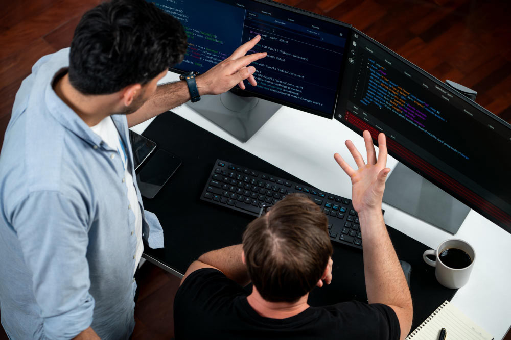 Dos desarrolladores revisando código en pantallas, comparando enfoques No Code y Low Code.