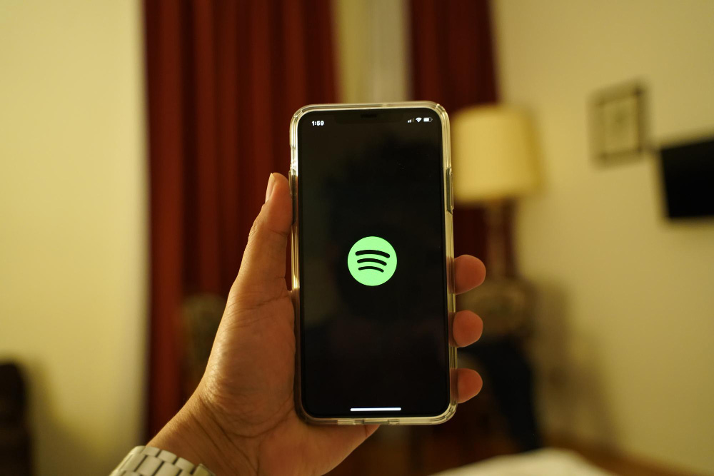 Persona sosteniendo un teléfono con la aplicación de Spotify abierta, simbolizando el papel de las plataformas en la distribución de música con IA.